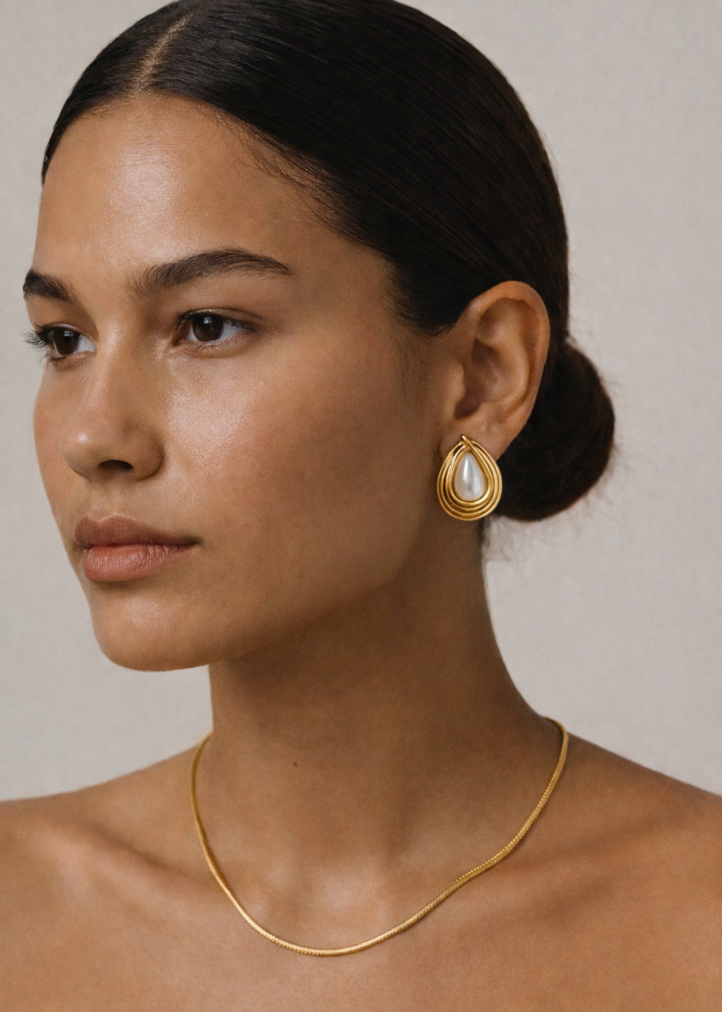 Woman wearing gold earrings and necklace against a neutral background