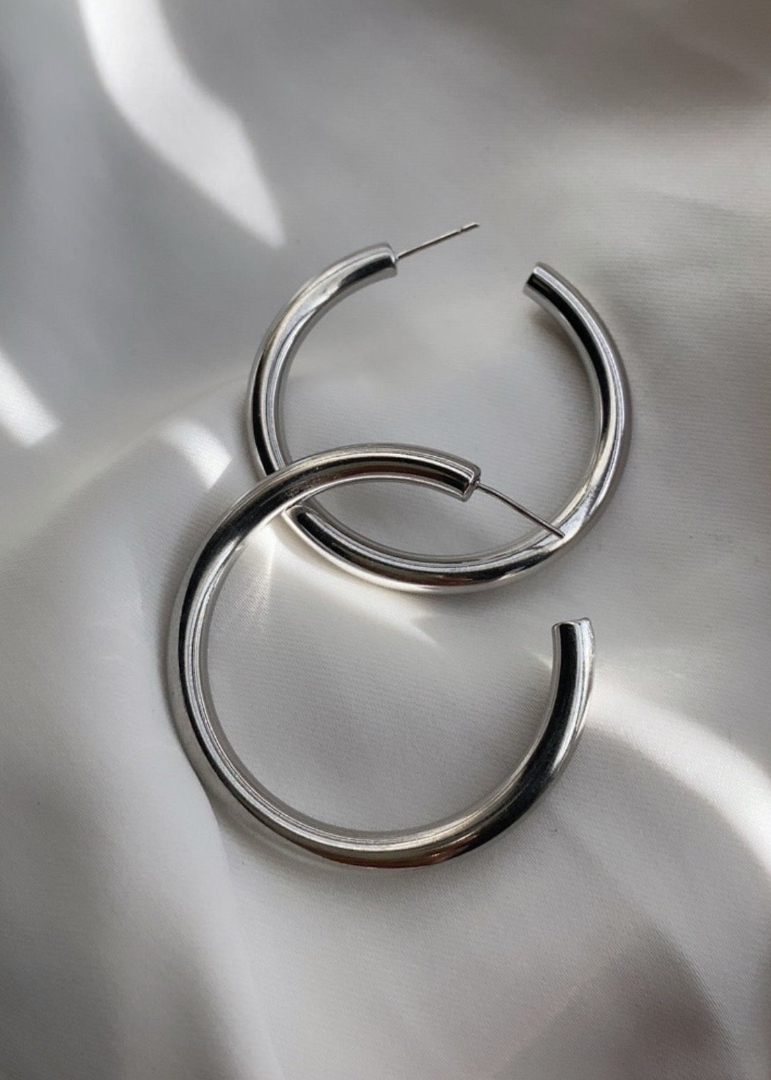 Pair of silver hoop earrings on a white fabric background