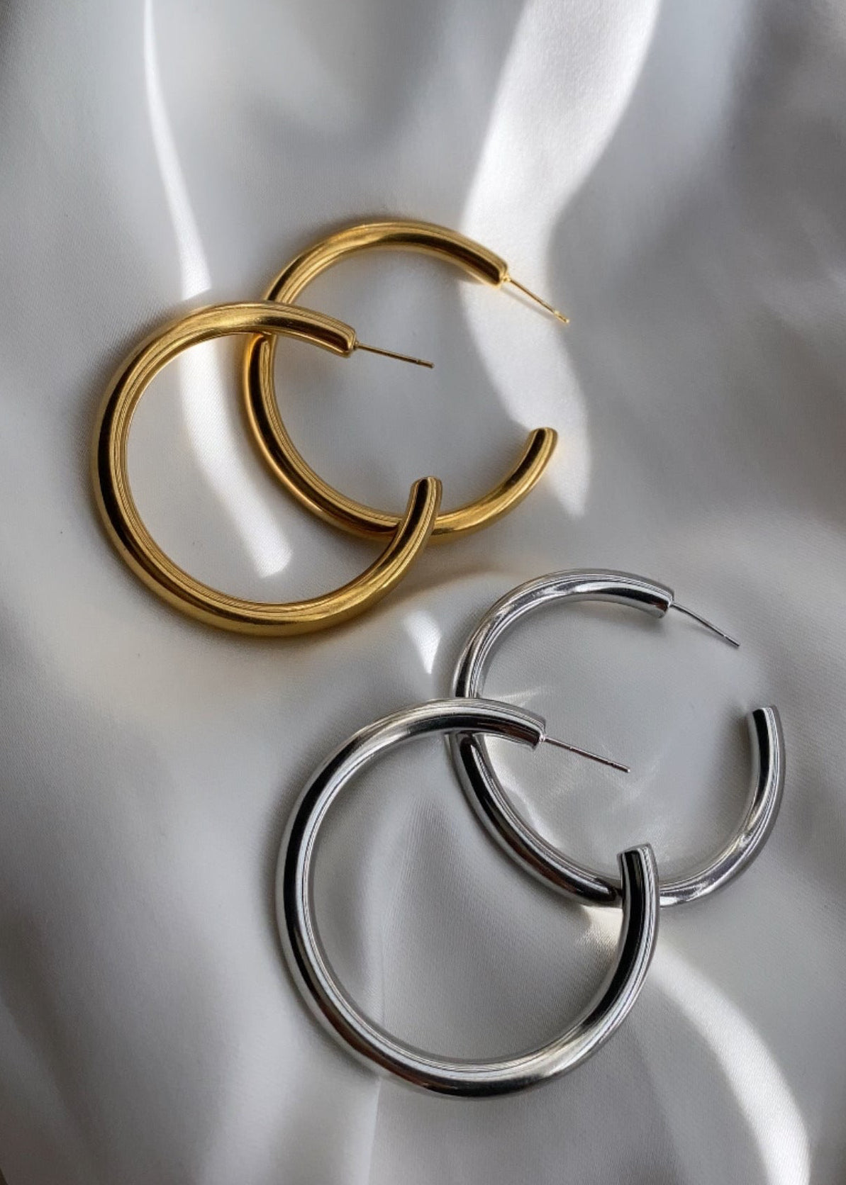 Gold and silver hoop earrings on a white fabric background
