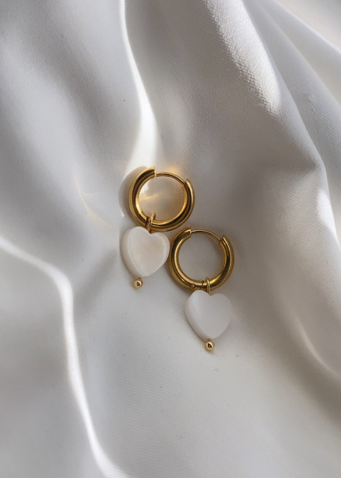 Gold and white earrings on a white fabric background