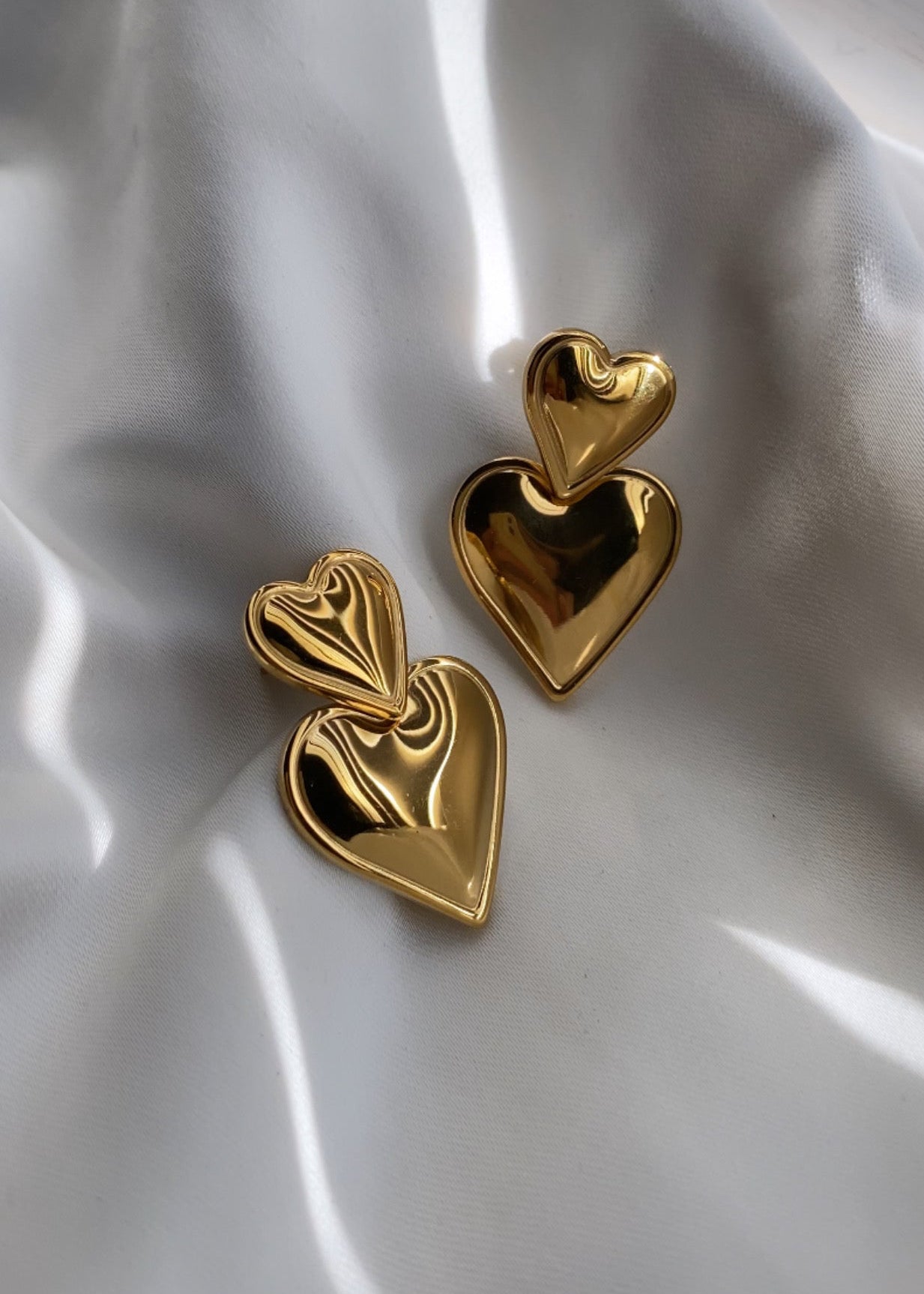 Gold heart-shaped earrings on a white fabric background