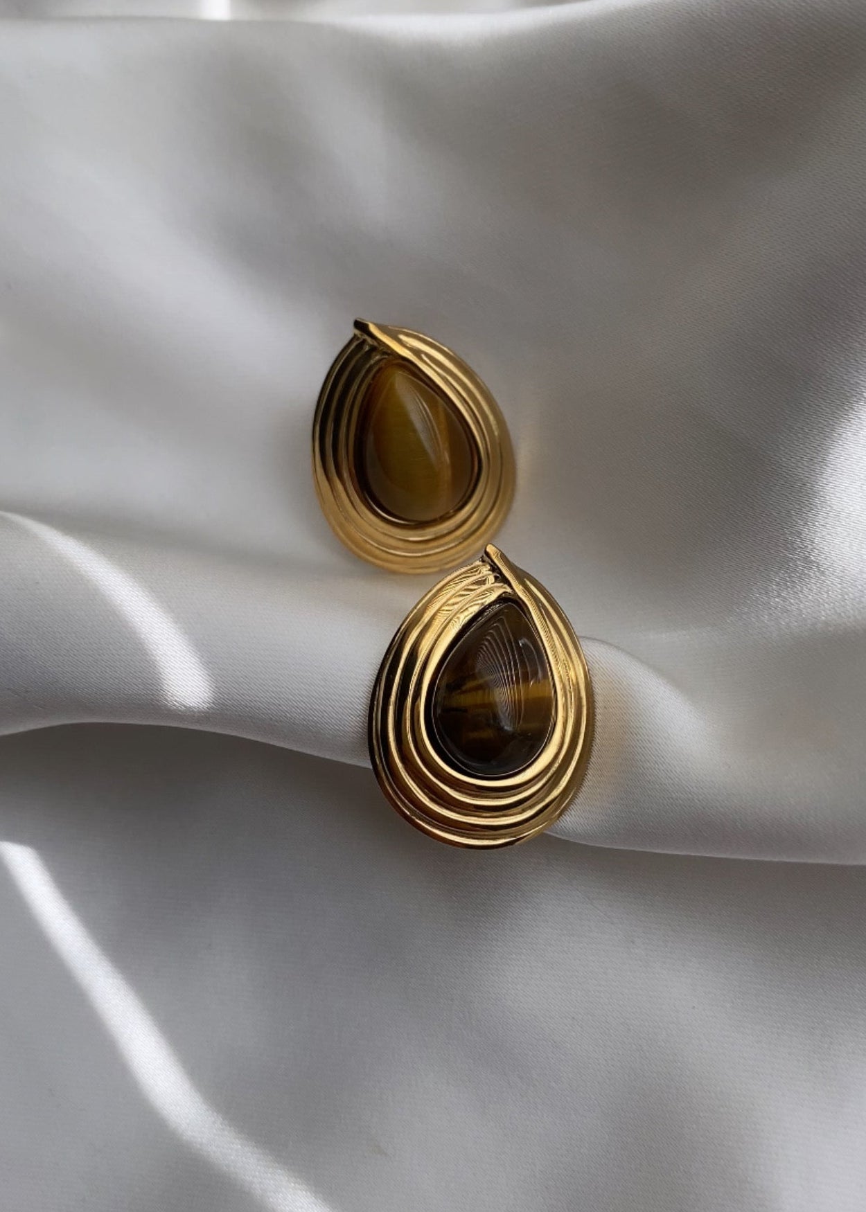Gold teardrop-shaped earrings on a white fabric background