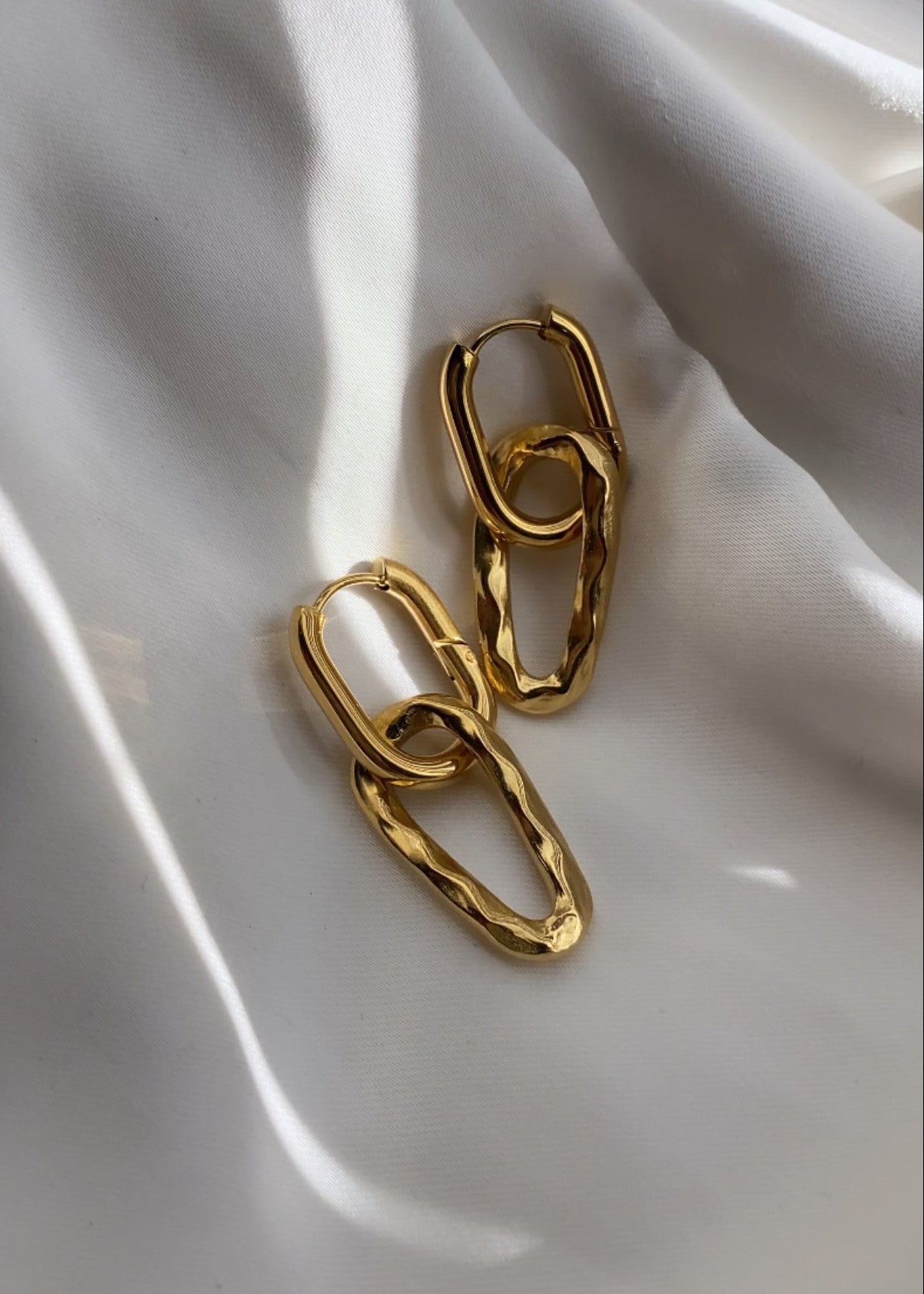 Gold chain earrings on a white fabric background