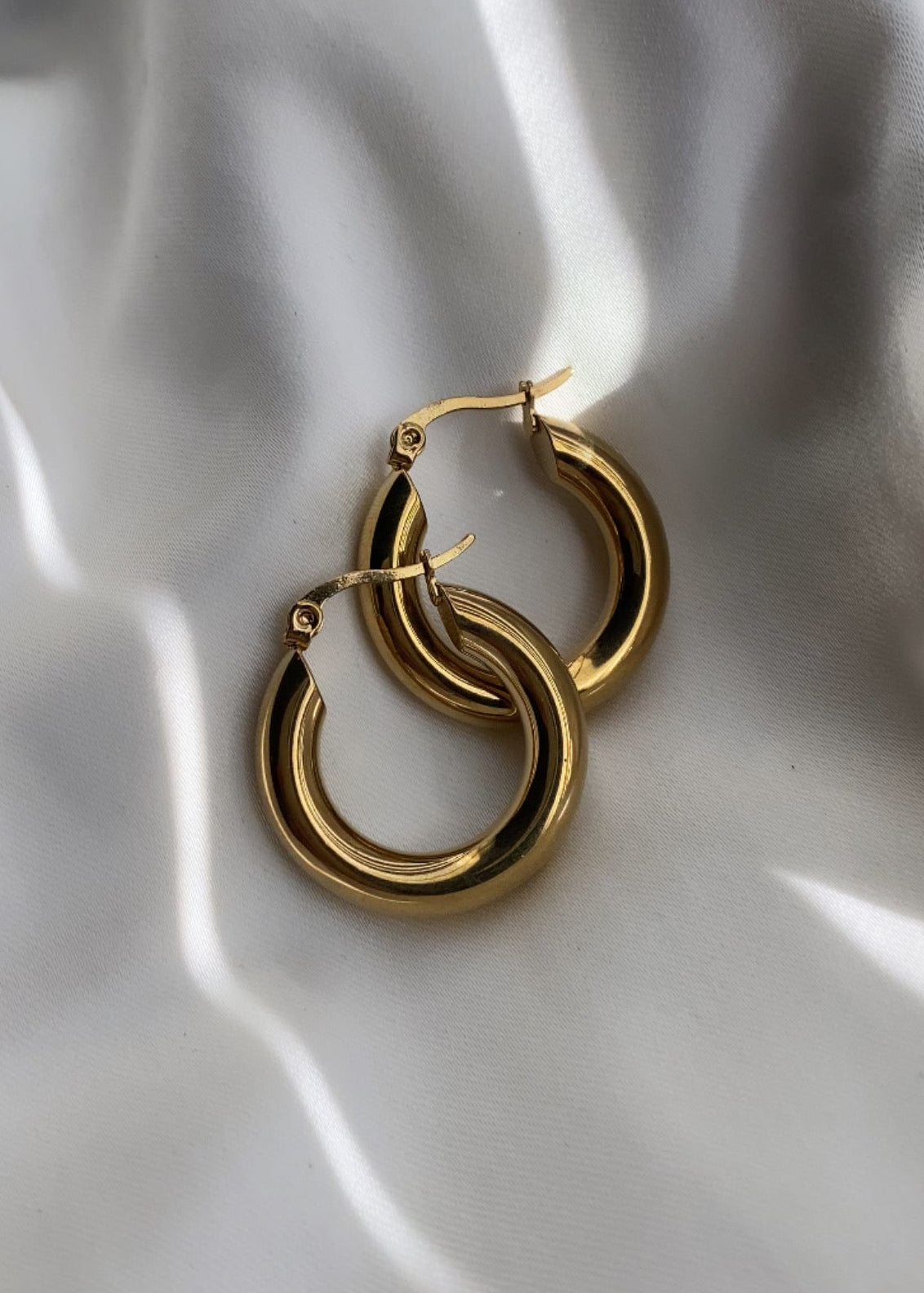 Gold hoop earrings on a white fabric background