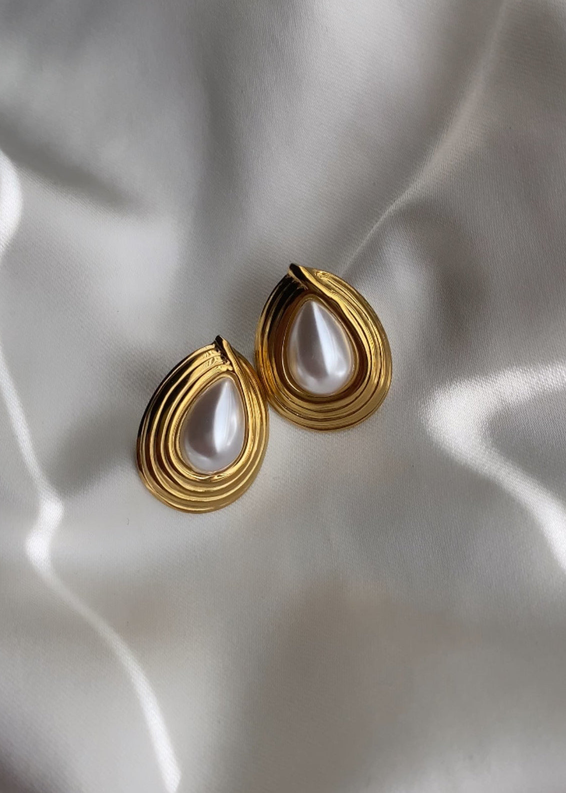 Gold earrings with pearl-like stones on a white fabric background
