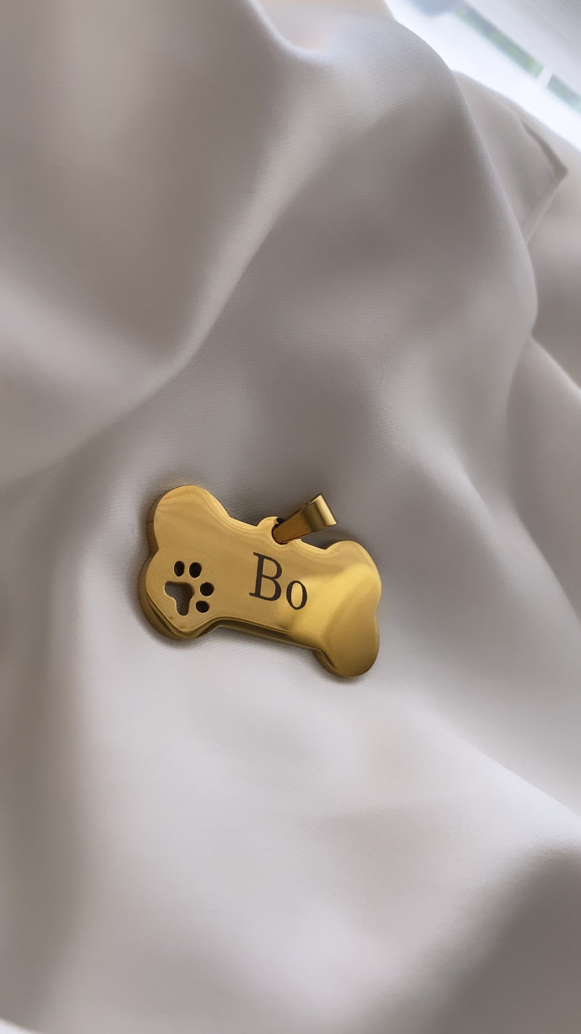 Gold dog tag with 'Bo' engraved on a light fabric background