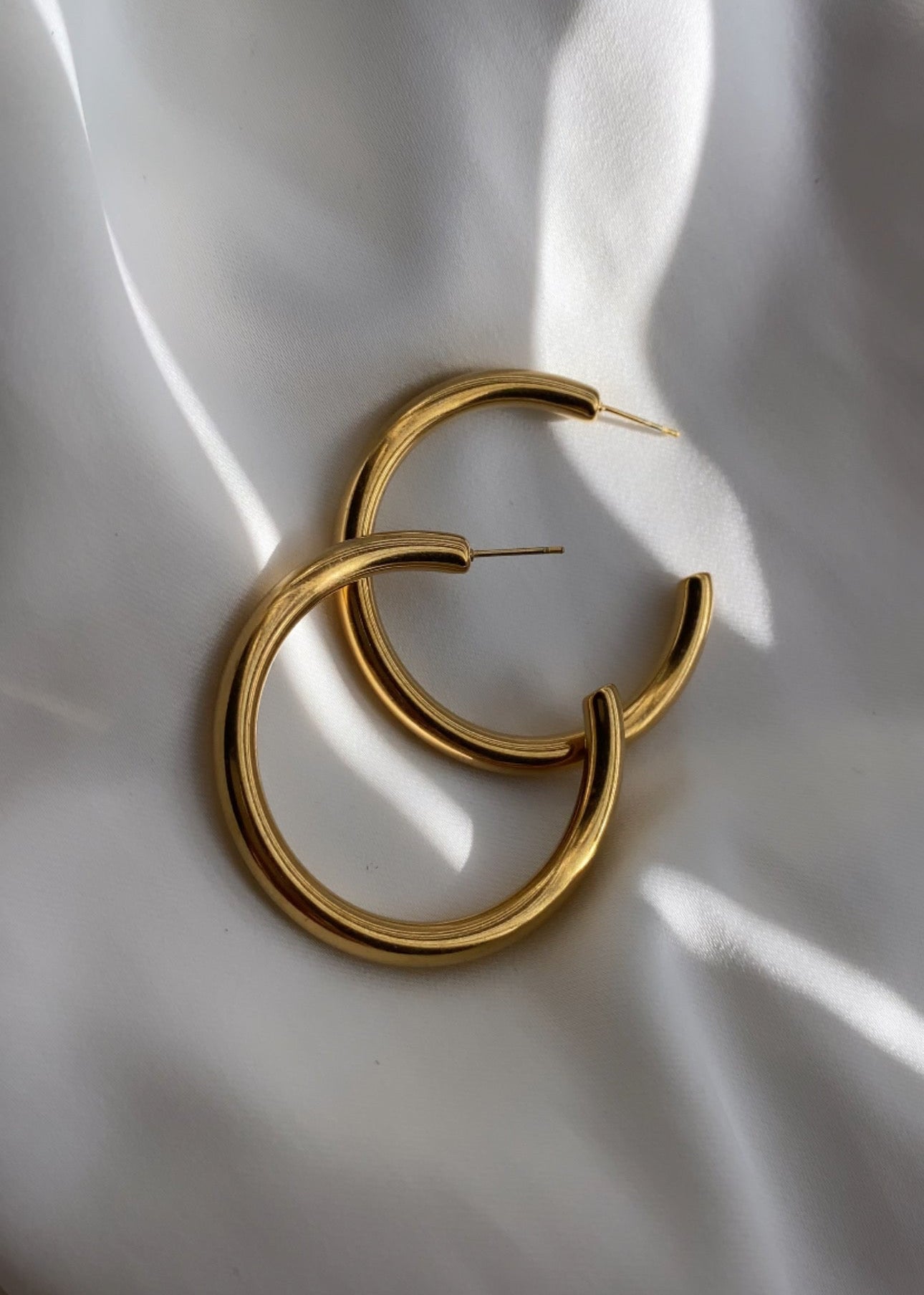 Gold hoop earrings on a white fabric background