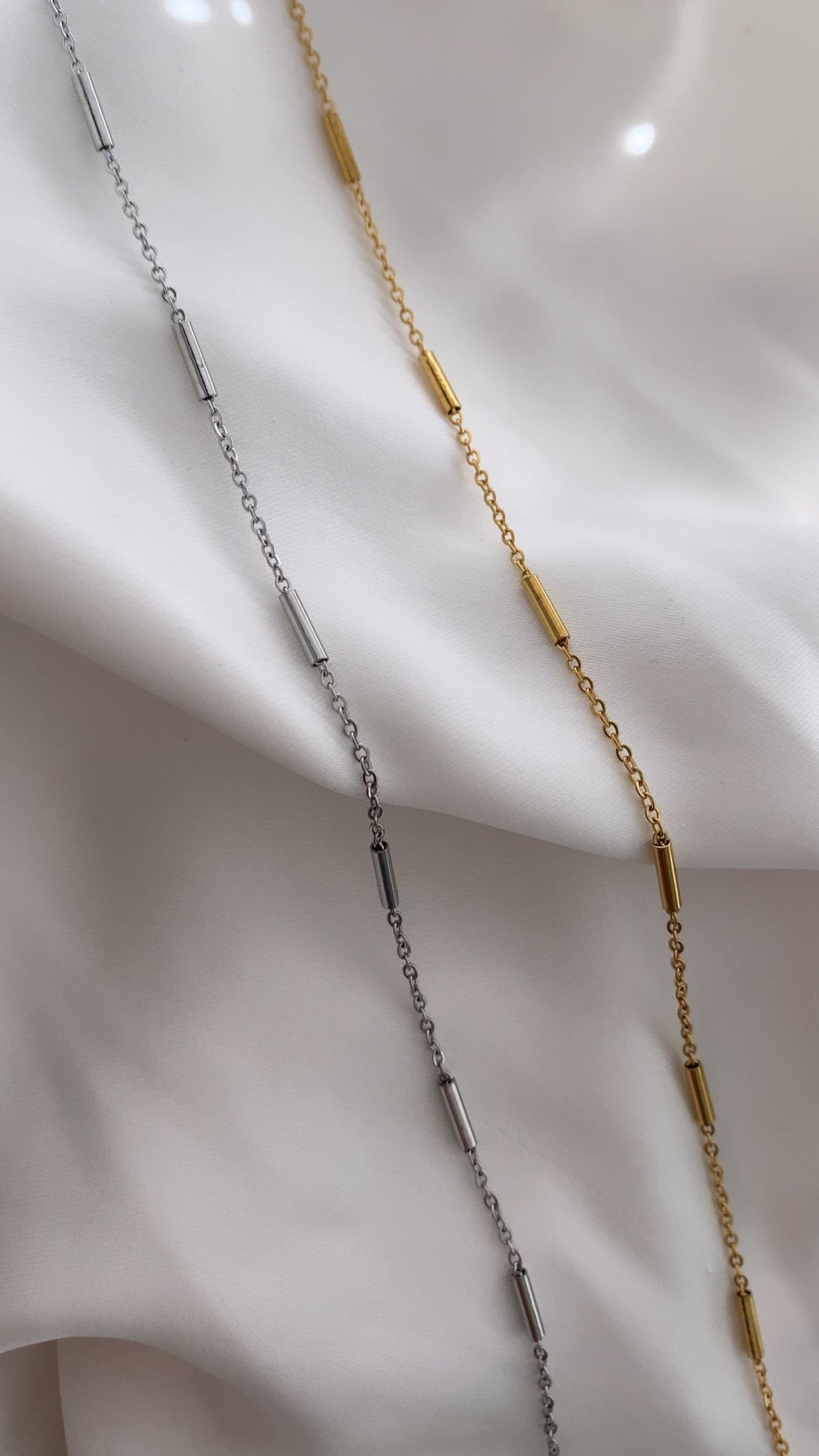 Two gold necklaces on a white fabric background