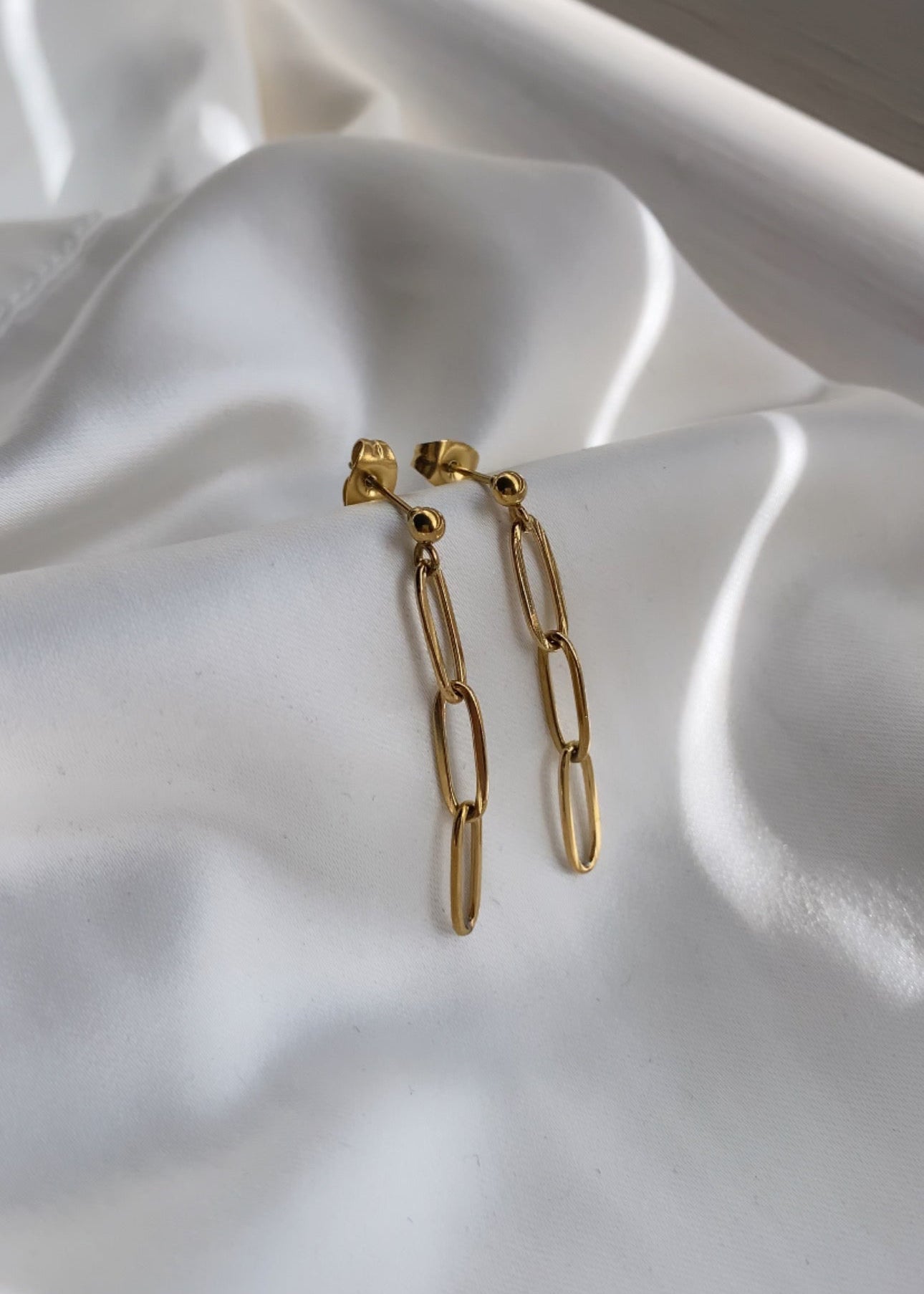 Gold chain earrings on a white fabric background