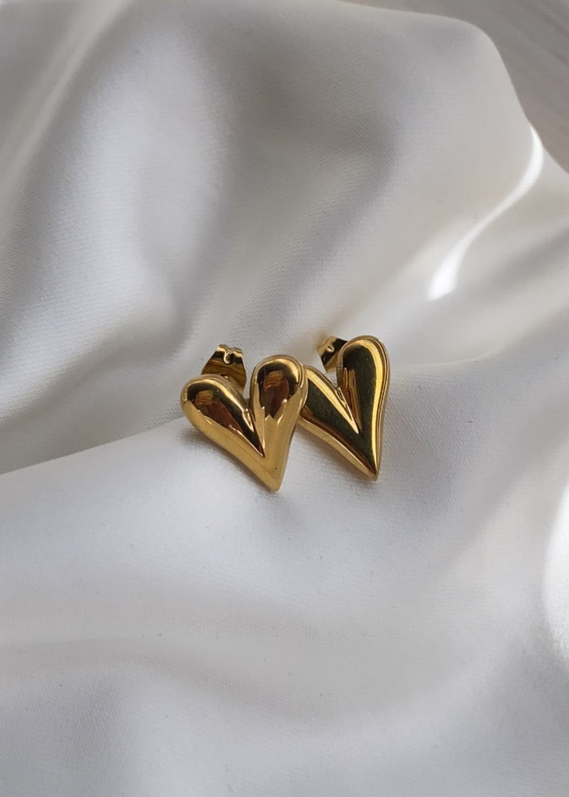 Gold heart-shaped earrings on a white fabric background