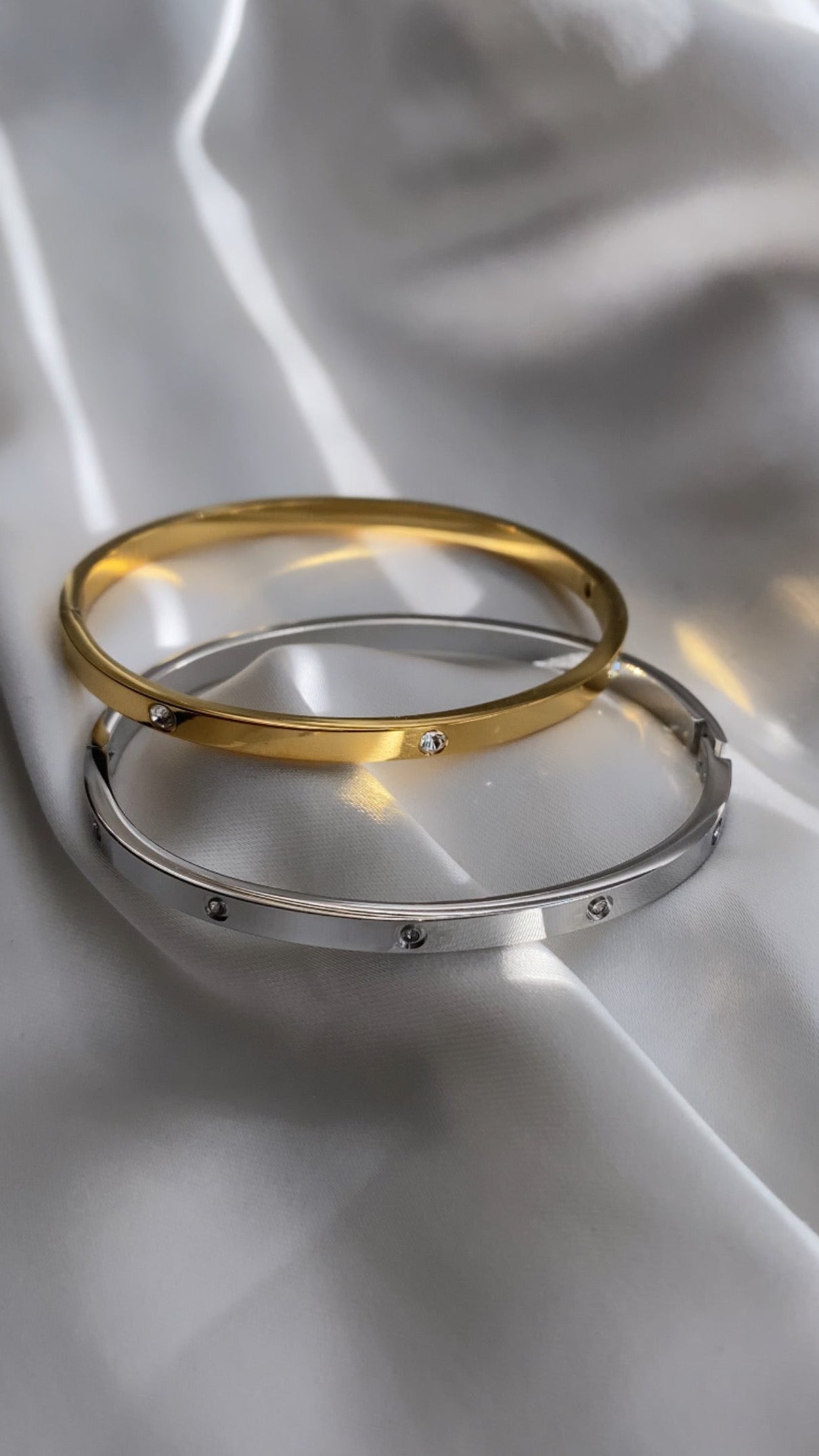 Two gold and silver bracelets on a white fabric background