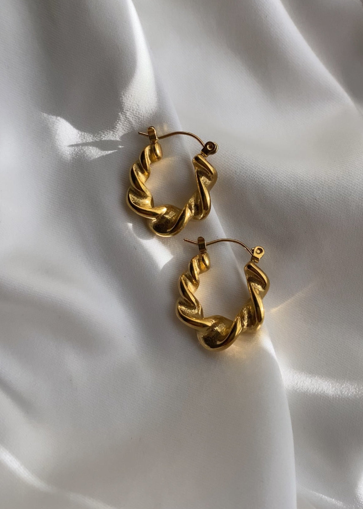 Gold hoop earrings on a white fabric background