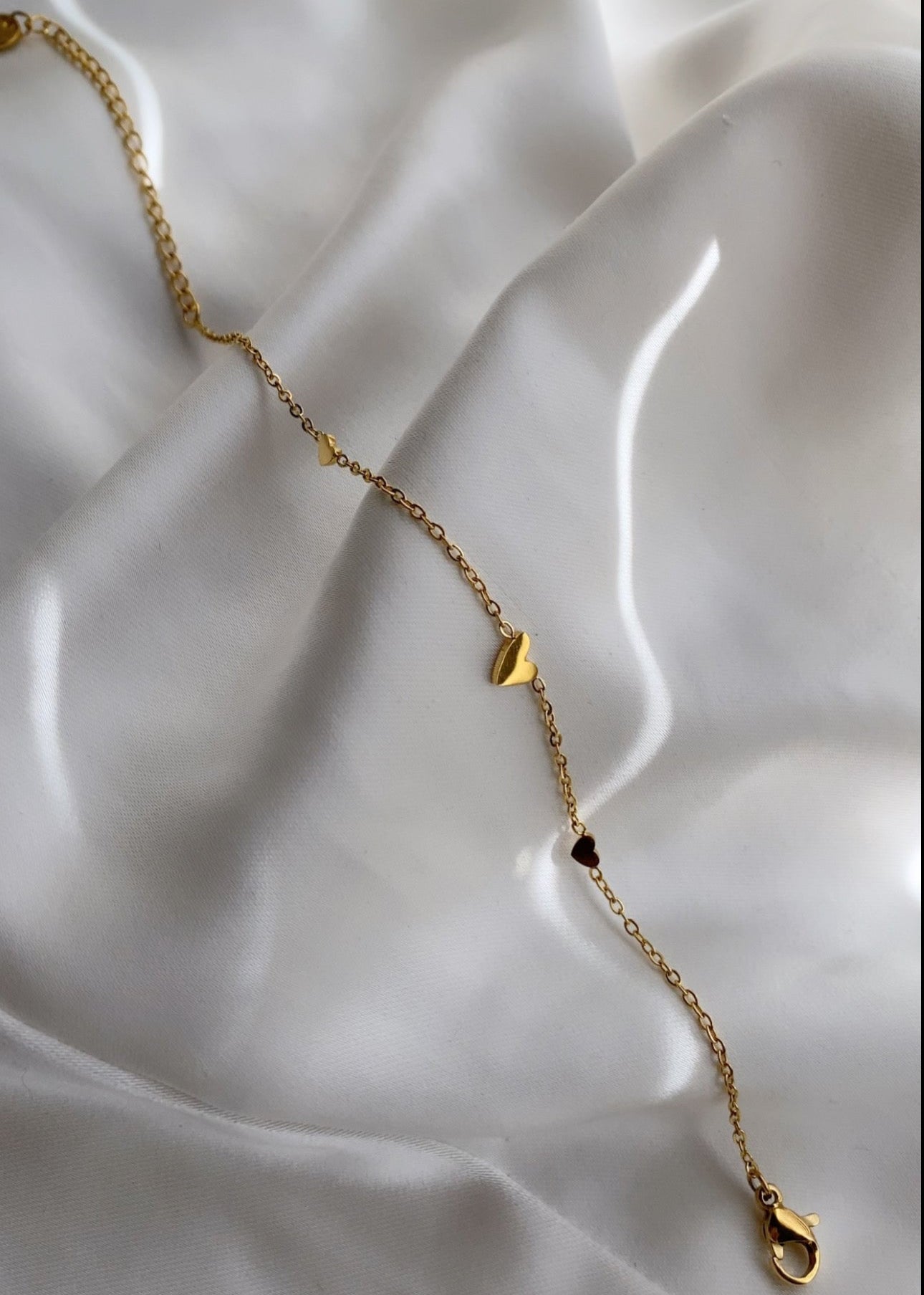 Gouden hand chain dames – fijne stainless steel handketting met kleine hartjes op ivoorkleurig satijn | Haydée Jewelry