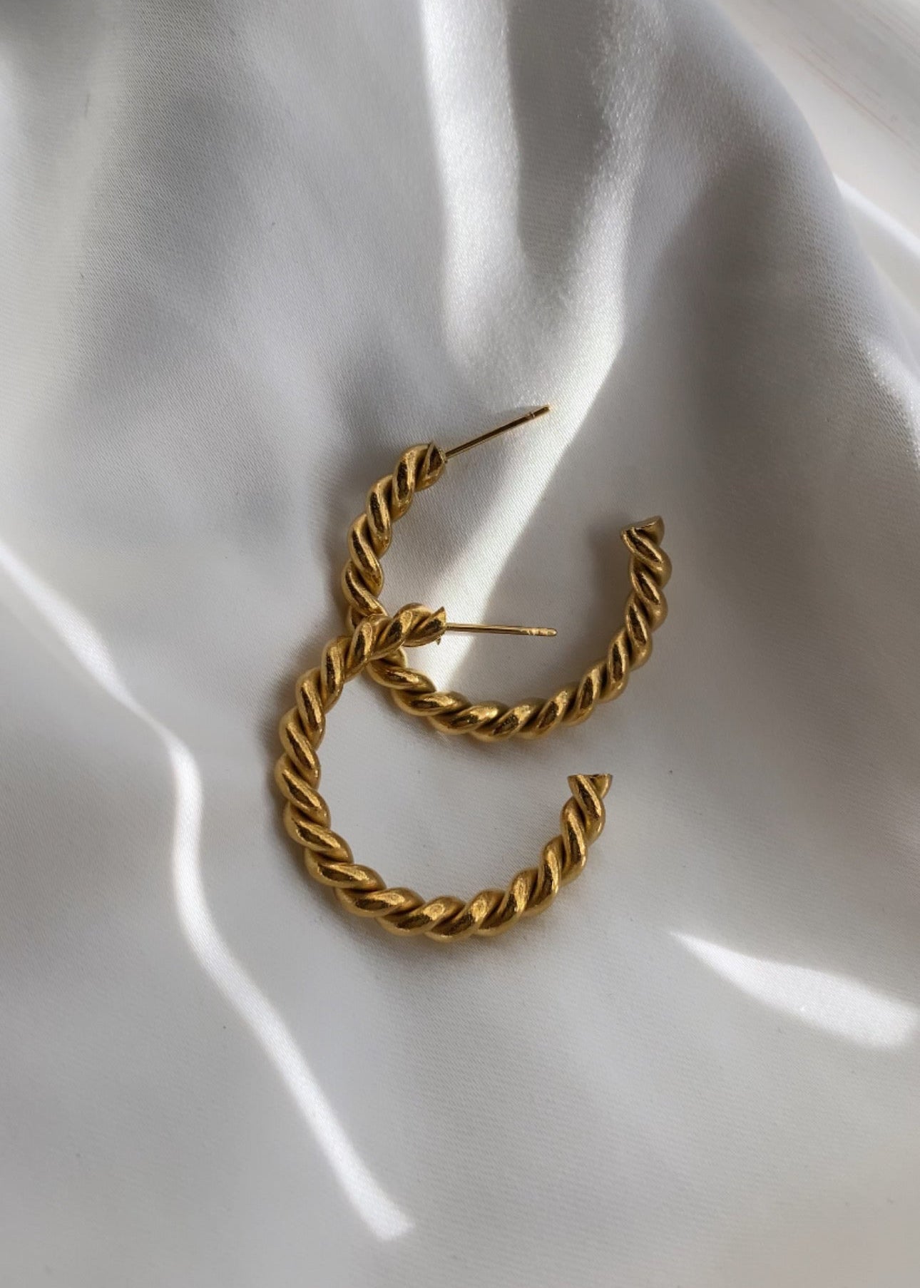 Gold hoop earrings on a white fabric background