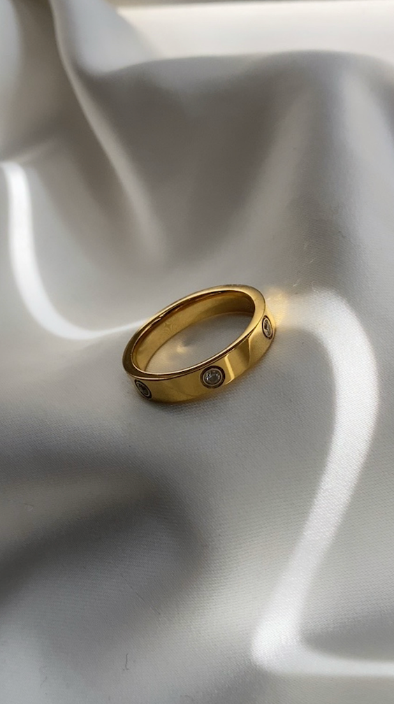 Gold ring with embedded stones on a white fabric background