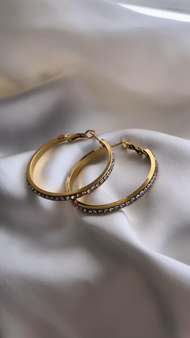 Gold hoop earrings with embedded stones on a soft fabric background