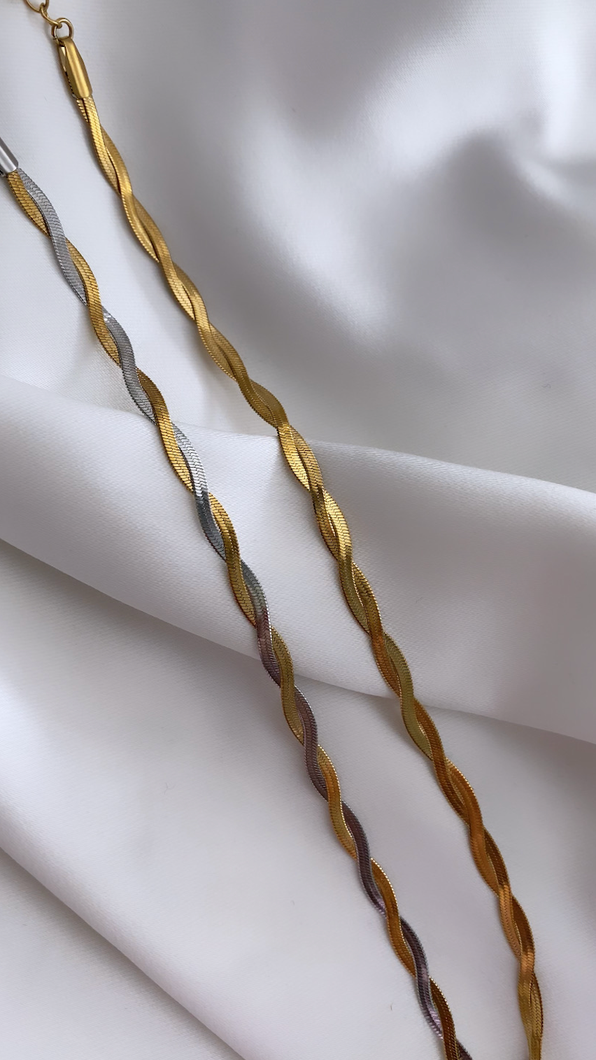 Gold and silver braided necklace on a white fabric background