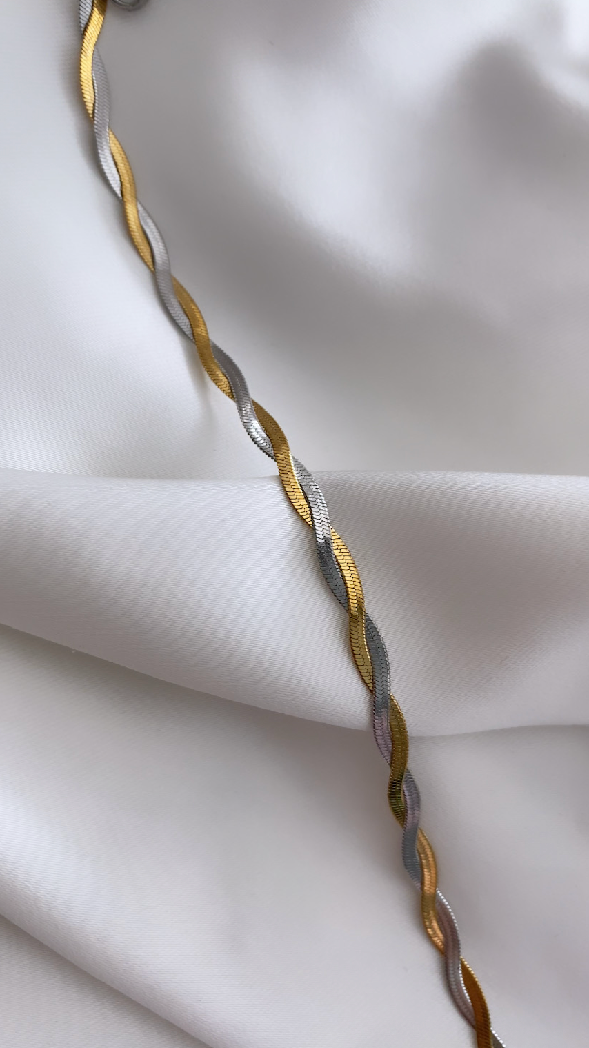 Gold and silver braided necklace on a white fabric background