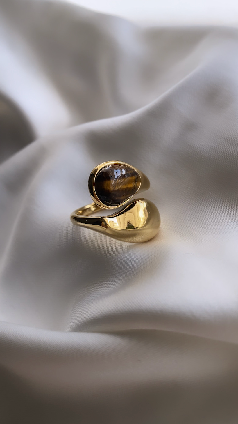 Gold ring with a dark stone on a white fabric background
