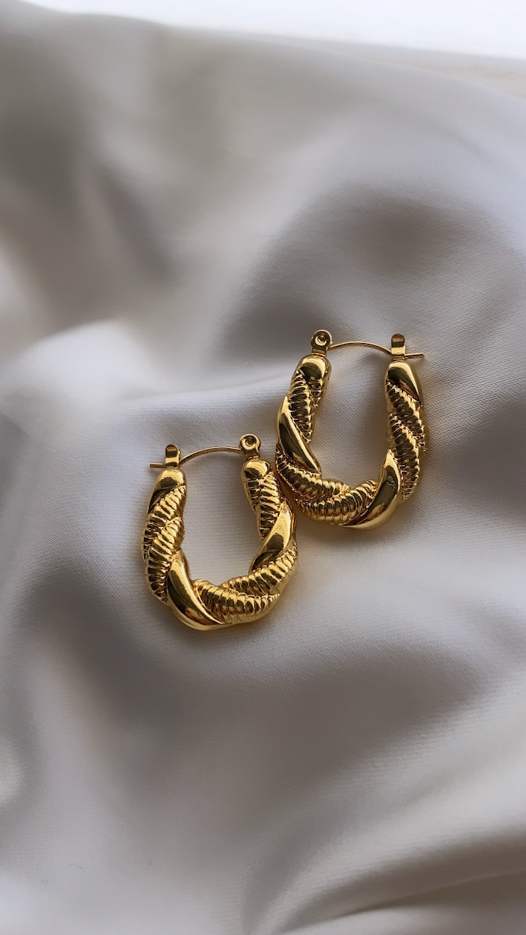 Gold hoop earrings on a white fabric background