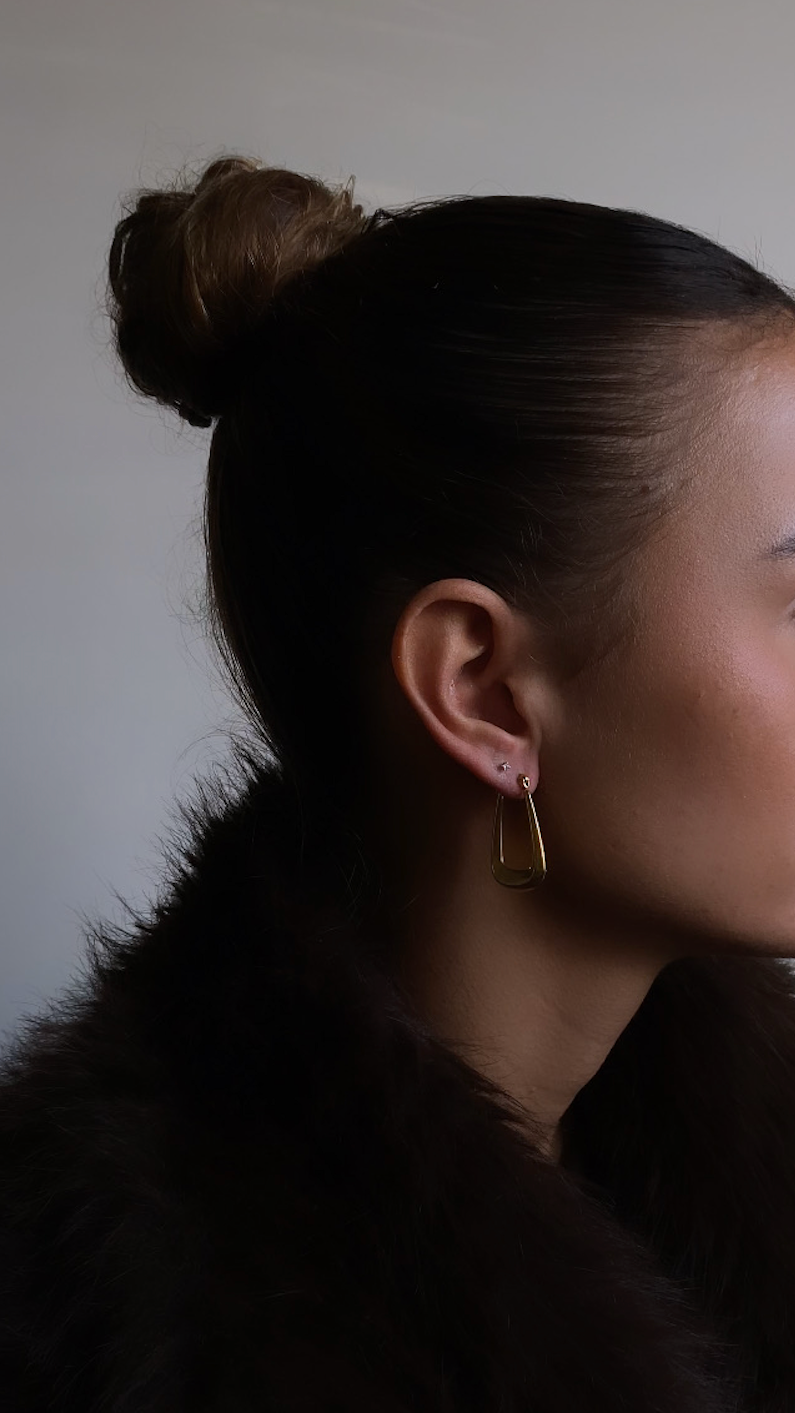Woman with a bun hairstyle wearing a dark fur coat and gold earring.