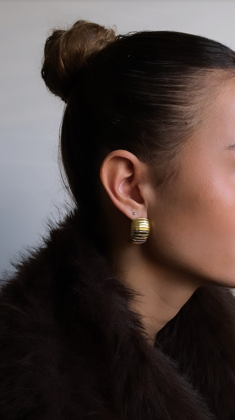 Woman wearing gold earrings with a fur coat against a neutral background