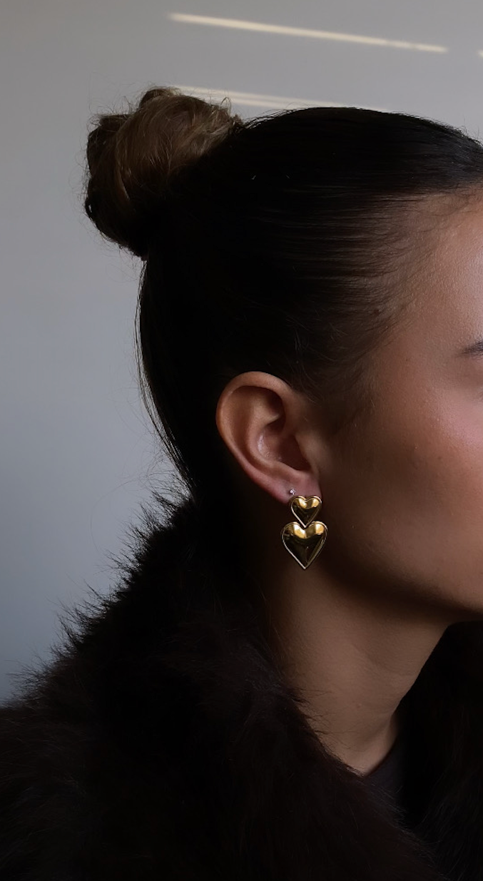 Woman with a bun hairstyle wearing gold earrings against a neutral background